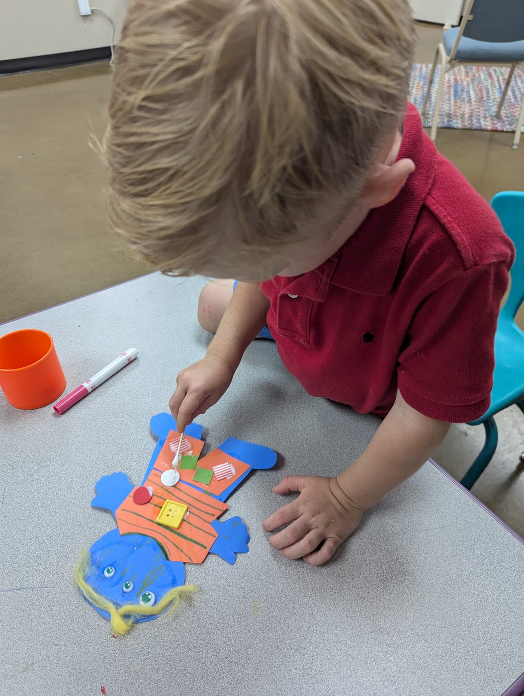 A boy gluing buttons and paper onto a collage figure