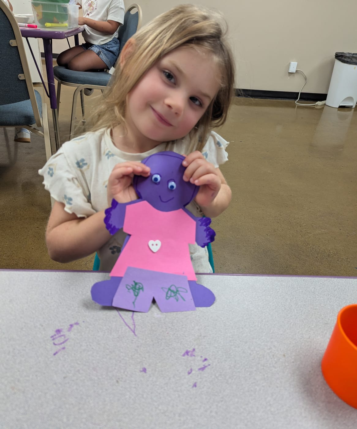A girl holding up the paper doll she made