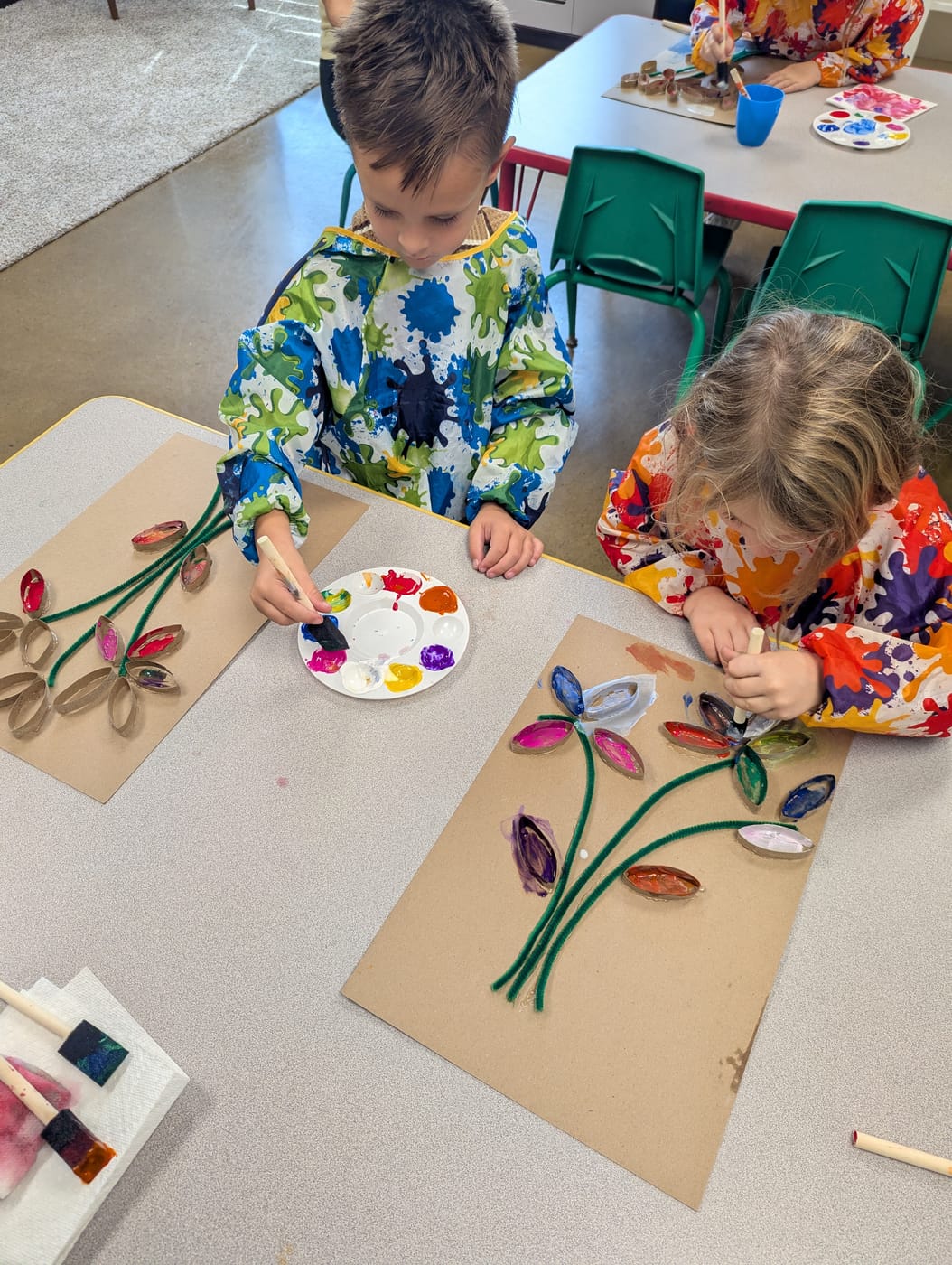 Two children painting cardboard-tube flowers in art class