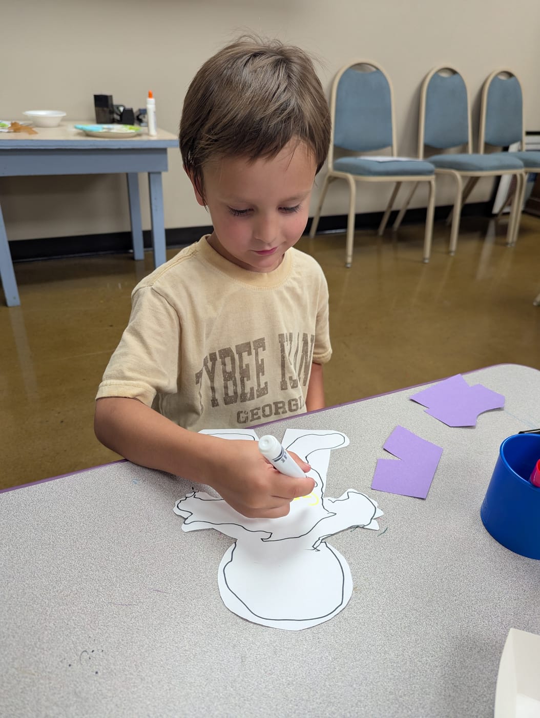 A boy decorating a paper cutout with a marker