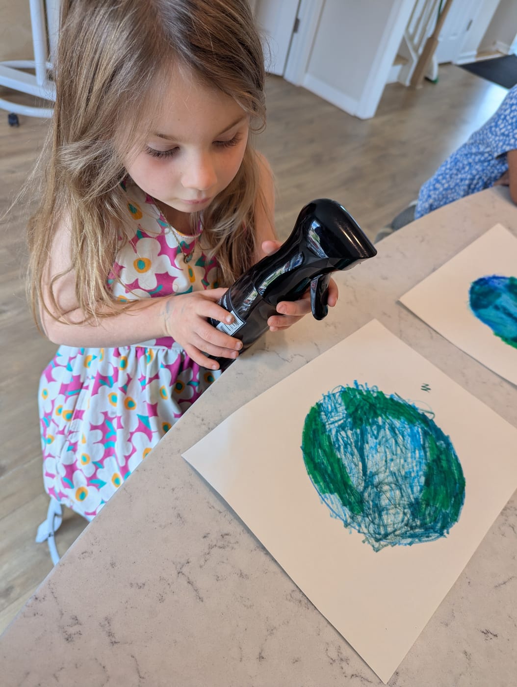 A girl spraying water on her crayon Earth drawing